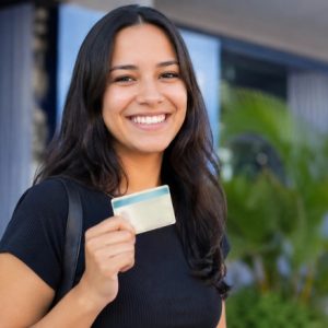 Uma pessoa sorridente comemora a conquista da CNH, segurando o documento com orgulho em um ambiente externo e institucional